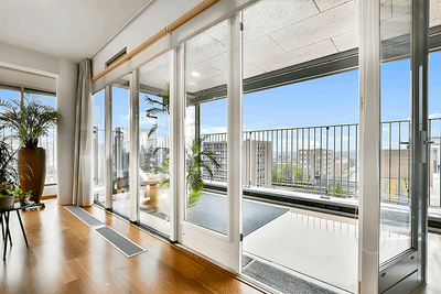 Interior view of modern living space with panoramic bi-fold doors opening to a balcony and city skyline.