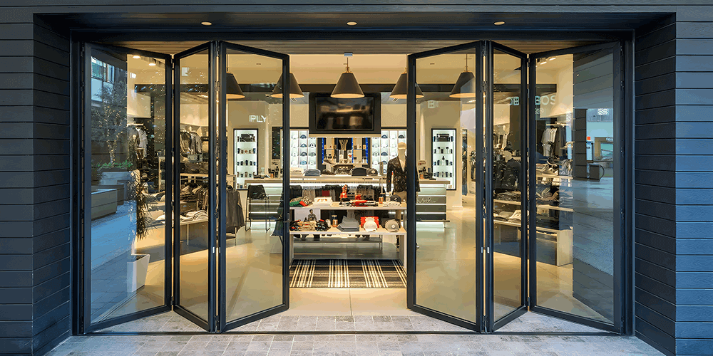 Stylish 16-foot wide bi-fold panoramic door opening to a modern retail store showcasing various products.